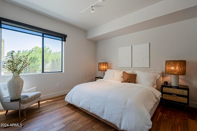 bedroom with dark hardwood / wood-style floors and track lighting