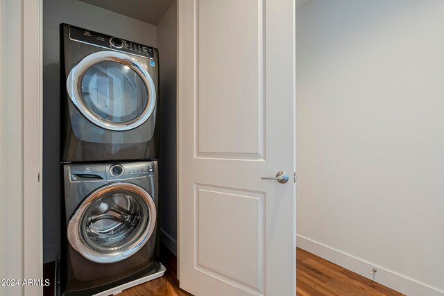 laundry area featuring stacked washer / dryer and dark hardwood / wood-style flooring