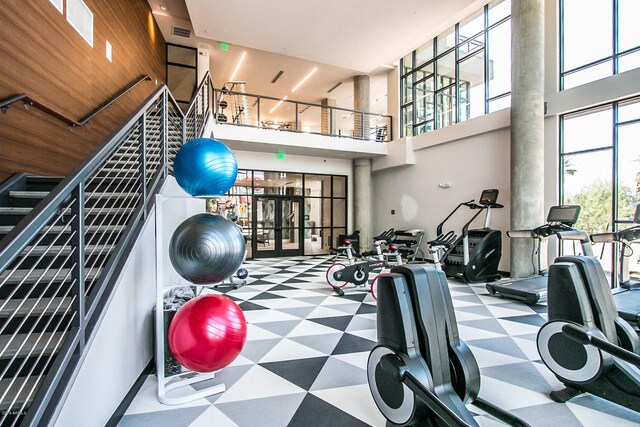 exercise room with light tile floors and a towering ceiling