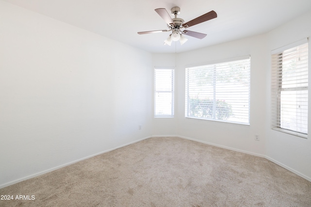 empty room featuring ceiling fan, light colored carpet, and plenty of natural light