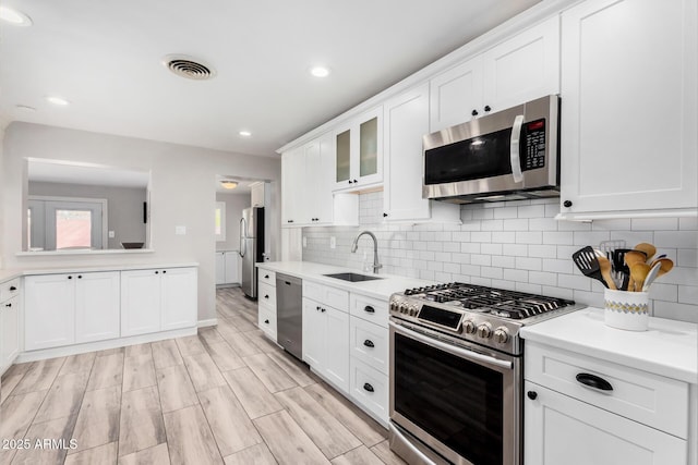 kitchen featuring sink, white cabinetry, tasteful backsplash, light wood-type flooring, and appliances with stainless steel finishes