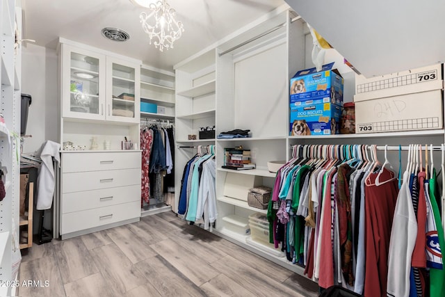 walk in closet featuring a notable chandelier and light hardwood / wood-style flooring