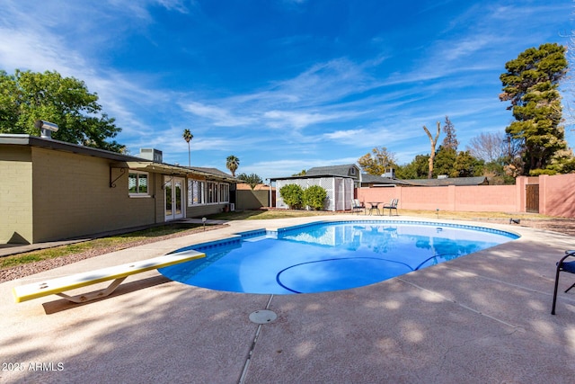 view of pool with a diving board, a patio area, and a storage shed