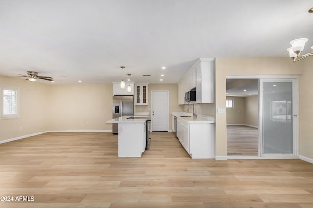 kitchen with white cabinets, a kitchen island, decorative light fixtures, stainless steel appliances, and light wood-type flooring