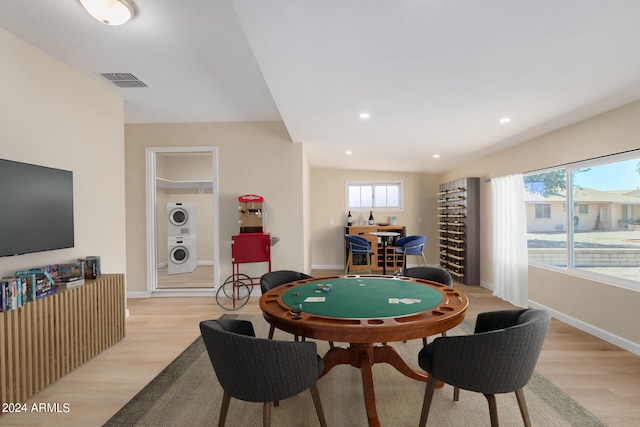 game room with light wood-type flooring, a healthy amount of sunlight, and stacked washer / drying machine