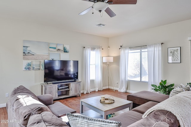 living room with ceiling fan, light wood finished floors, visible vents, and baseboards