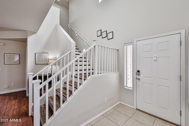 foyer entrance featuring a towering ceiling, stairway, baseboards, and tile patterned floors