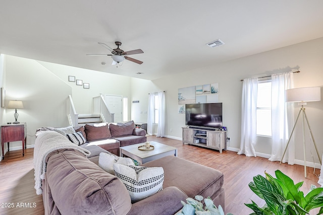 living room with light wood-style flooring, visible vents, baseboards, stairs, and a ceiling fan