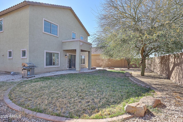 rear view of house with a fenced backyard, a yard, a tiled roof, and stucco siding