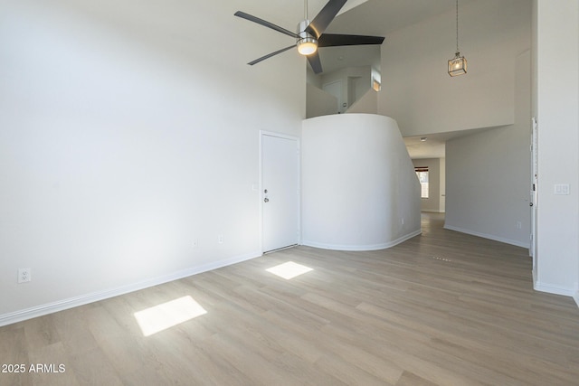 unfurnished living room featuring ceiling fan, a towering ceiling, and wood-type flooring