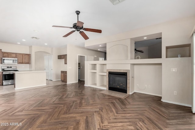 12814 W Indianola Ave, Avondale, AZ 85392 - unfurnished living room featuring baseboards, a tiled fireplace, a ceiling fan, visible vents, and arched walkways