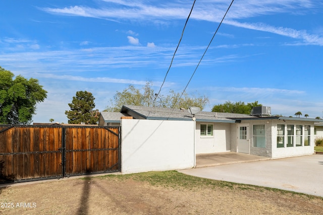 back of property featuring a gate, central AC unit, a patio area, fence, and stucco siding