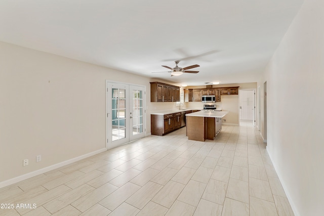 kitchen featuring stainless steel appliances, light countertops, a sink, a kitchen island, and ceiling fan