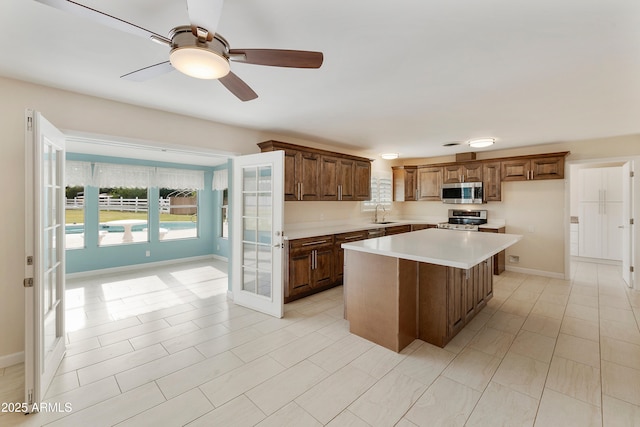 kitchen with stainless steel appliances, light countertops, a ceiling fan, a kitchen island, and baseboards
