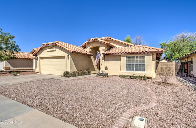 mediterranean / spanish house with fence, a tiled roof, concrete driveway, stucco siding, and a garage