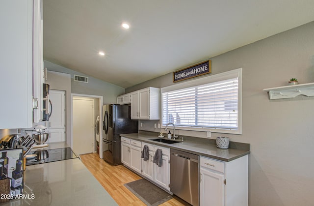 kitchen featuring visible vents, a sink, stainless steel dishwasher, white cabinetry, and freestanding refrigerator