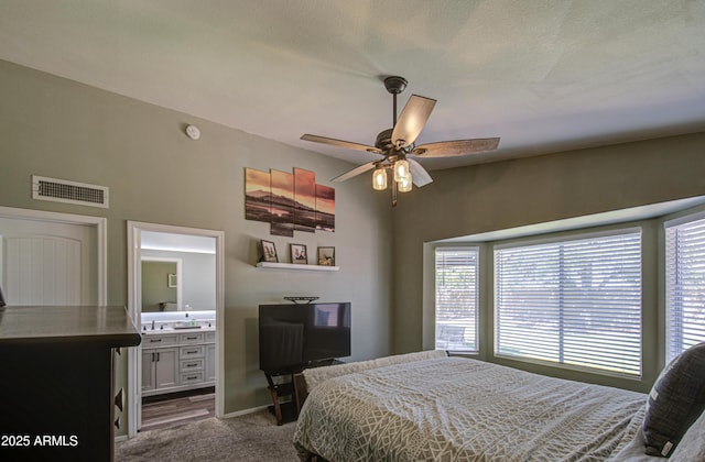 bedroom with visible vents, a ceiling fan, ensuite bath, dark carpet, and baseboards