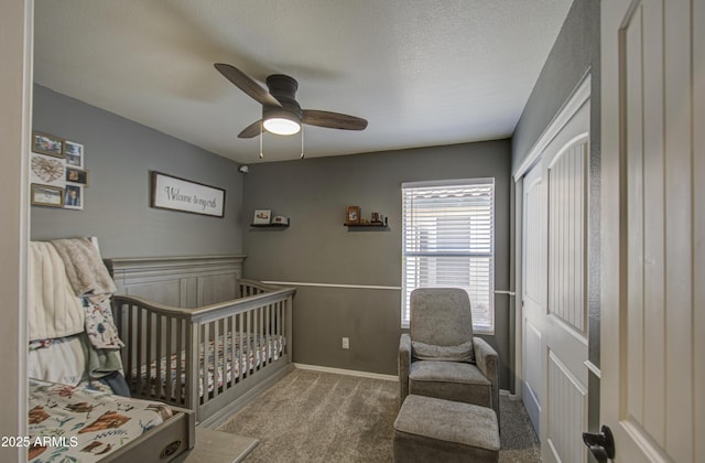 carpeted bedroom with a crib, ceiling fan, a wainscoted wall, a closet, and a textured ceiling