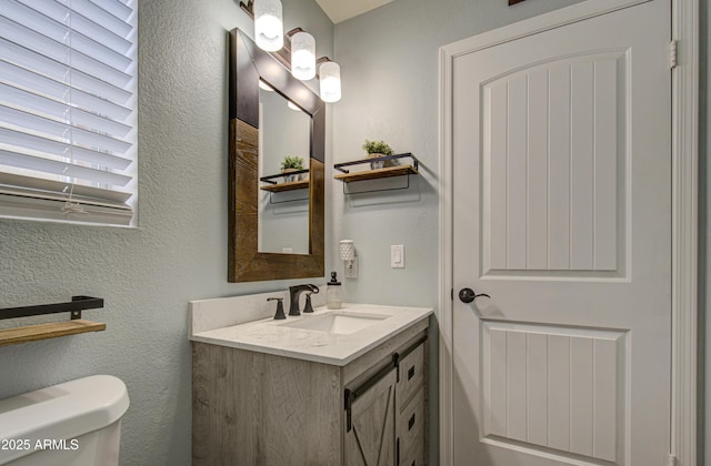 bathroom featuring toilet, vanity, and a textured wall