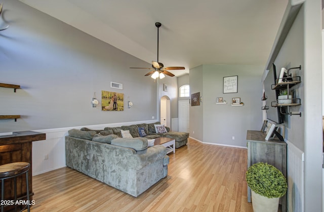 living area featuring visible vents, ceiling fan, light wood-type flooring, wainscoting, and arched walkways