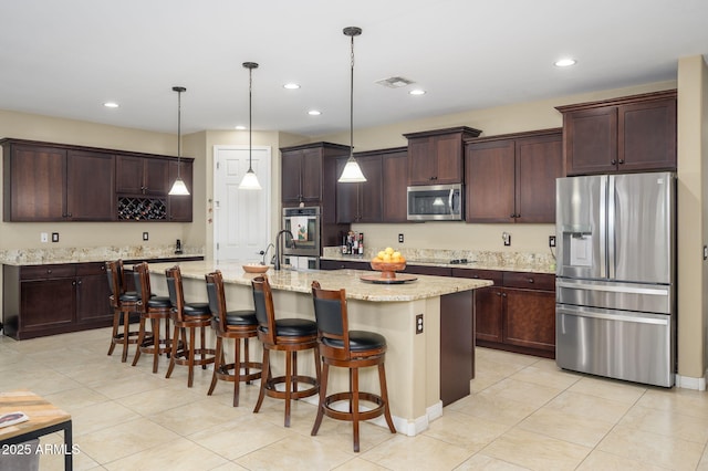 kitchen featuring visible vents, appliances with stainless steel finishes, a kitchen bar, dark brown cabinets, and a center island with sink