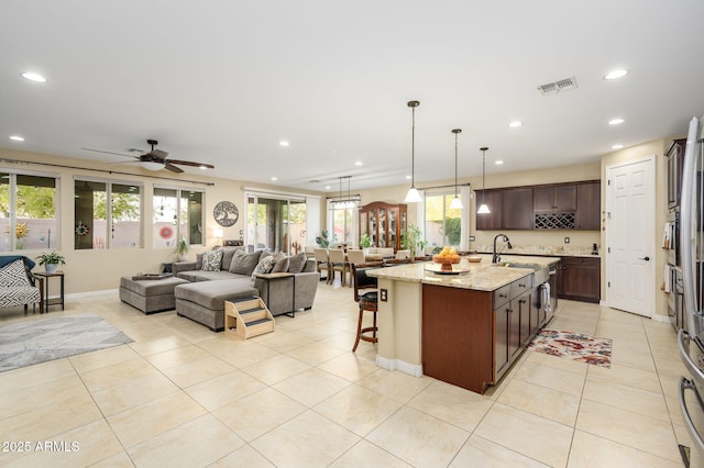 kitchen with light tile patterned floors, dark brown cabinets, a ceiling fan, a breakfast bar, and open floor plan