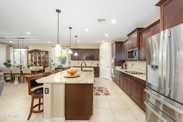 kitchen with visible vents, light tile patterned floors, a breakfast bar, a center island with sink, and stainless steel appliances