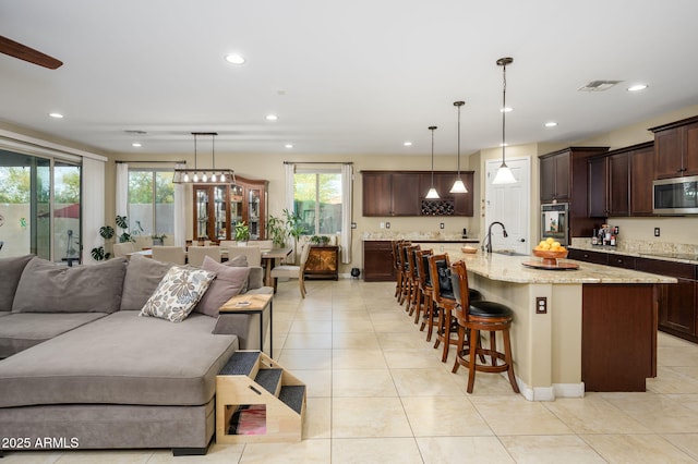 kitchen featuring dark brown cabinets, light stone counters, stainless steel microwave, a sink, and open floor plan