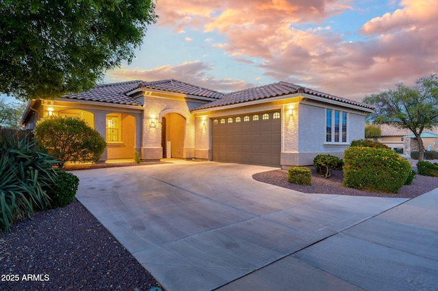 mediterranean / spanish-style home featuring a tiled roof, a garage, stucco siding, and driveway