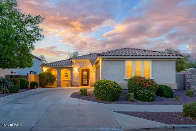mediterranean / spanish home with a tile roof, fence, stucco siding, and concrete driveway