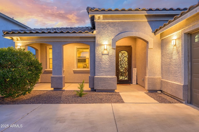 exterior entry at dusk featuring stucco siding and a tile roof