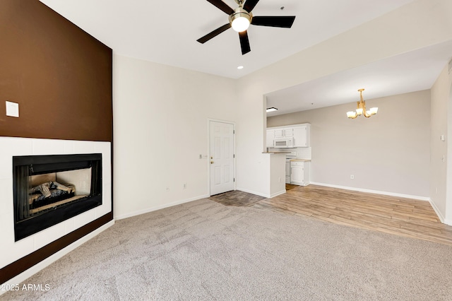 unfurnished living room with a tile fireplace, light carpet, and ceiling fan with notable chandelier