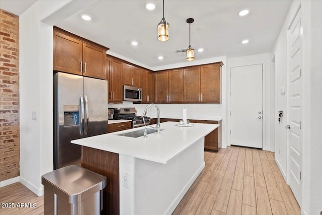 kitchen with appliances with stainless steel finishes, pendant lighting, a sink, and light wood finished floors