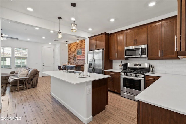 kitchen featuring open floor plan, light wood-type flooring, light countertops, a sink, and appliances with stainless steel finishes