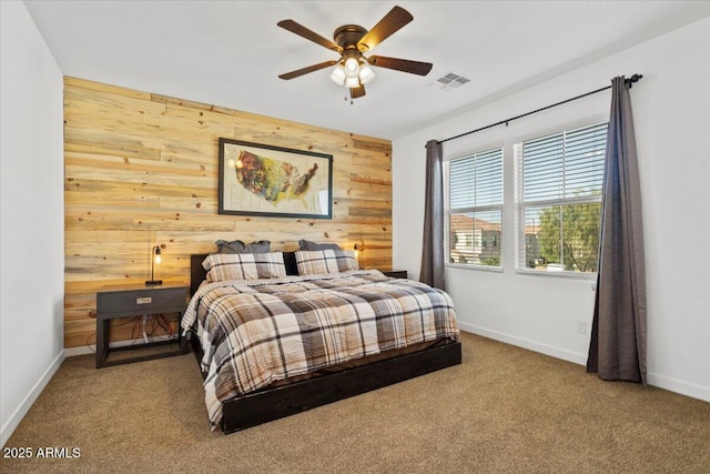 carpeted bedroom featuring visible vents, a ceiling fan, baseboards, and wooden walls