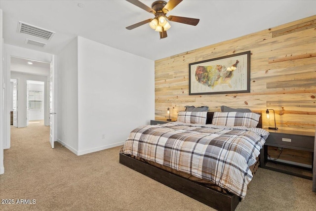 carpeted bedroom with wooden walls, baseboards, visible vents, and ceiling fan
