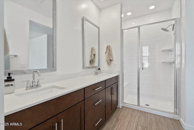 full bathroom with double vanity, a shower stall, a sink, and wood finished floors