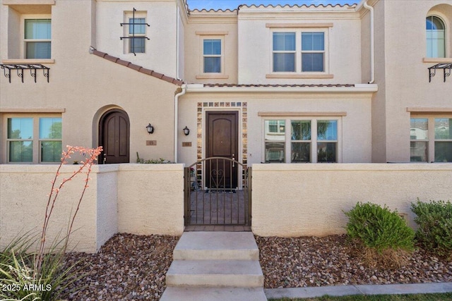 multi unit property featuring a tiled roof, a fenced front yard, a gate, and stucco siding