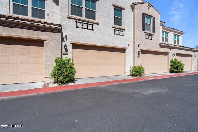 multi unit property with a garage, stucco siding, and a tile roof