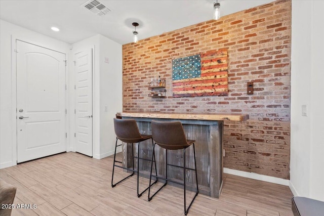 bar with baseboards, visible vents, a bar, and light wood-type flooring