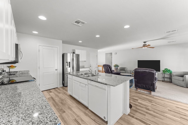 kitchen with stainless steel appliances, white cabinets, ceiling fan, light stone countertops, and a center island with sink