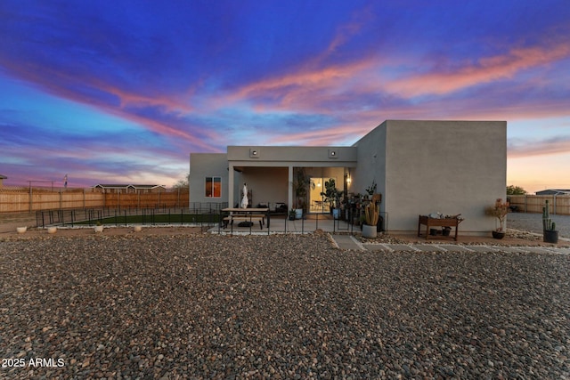 back of property at dusk with a patio area, stucco siding, and a fenced backyard