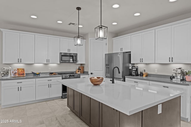 kitchen featuring an island with sink, white cabinetry, visible vents, stainless steel appliances, and a sink