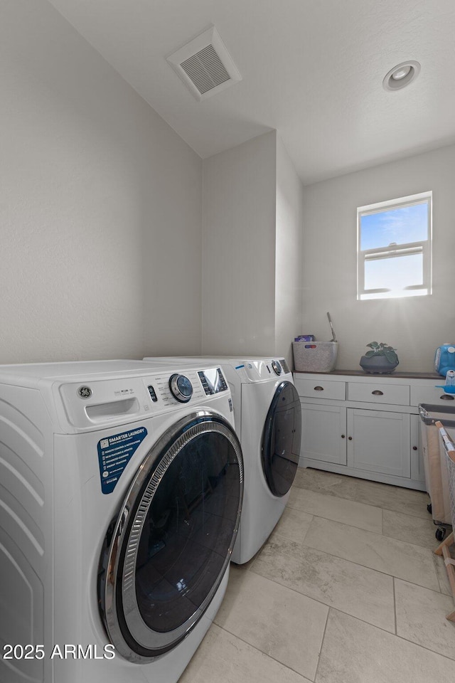 clothes washing area with washing machine and clothes dryer, cabinet space, and visible vents