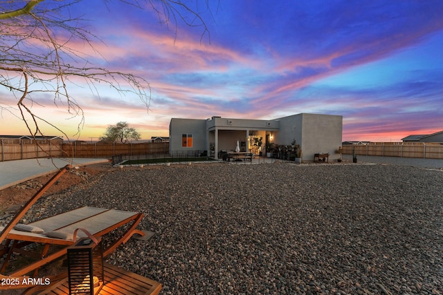 back of house at dusk with a fenced backyard, stucco siding, and a patio area