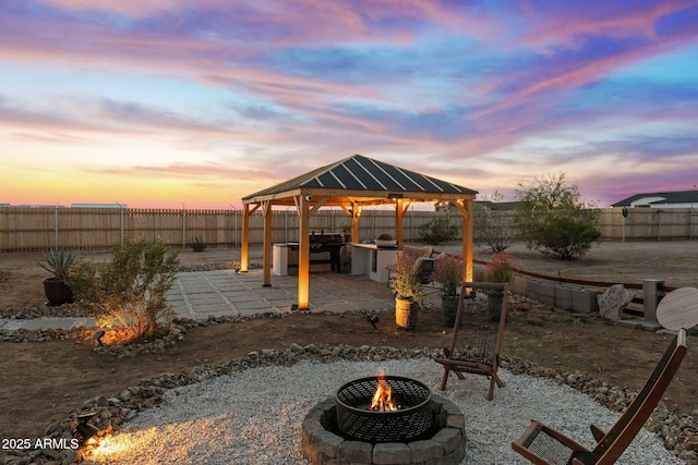 patio terrace at dusk featuring a gazebo, a fenced backyard, and an outdoor fire pit