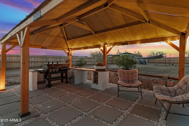patio terrace at dusk with area for grilling, a gazebo, and fence