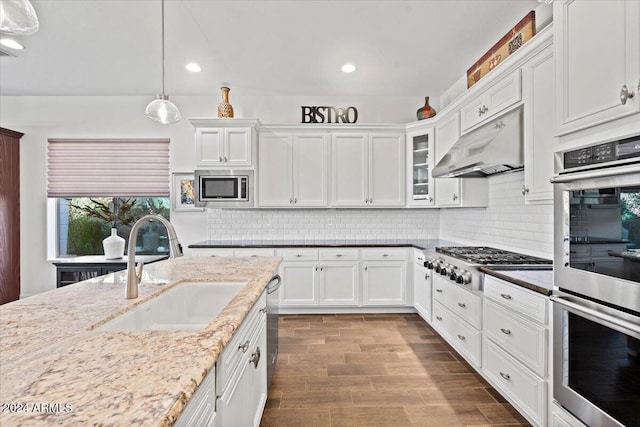 kitchen featuring sink, range hood, pendant lighting, white cabinets, and appliances with stainless steel finishes