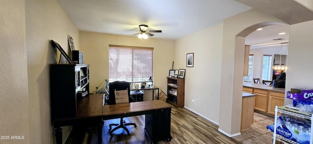 home office with light wood-type flooring, visible vents, arched walkways, baseboards, and ceiling fan