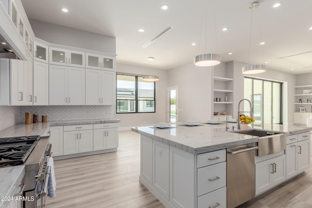 kitchen with white cabinetry, an island with sink, light wood-type flooring, decorative light fixtures, and sink